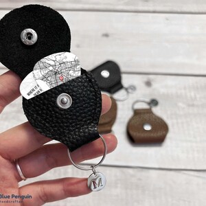 Puede incluir: Portapleitas de cuero negro con un mapa de "Where it all began" en su interior. El portapleitas tiene un cierre a presión y un llavero plateado con un dije plateado que dice "M".