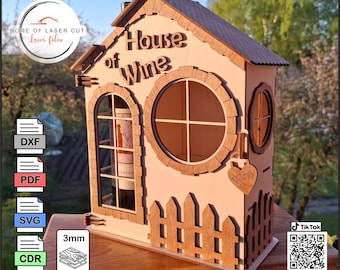 May include: Wooden house-shaped wine rack with the words "House of Wine" cut out. Features a round window, arched window, and a small heart-shaped tag that says "Wine". Includes a picket fence design at the base.
