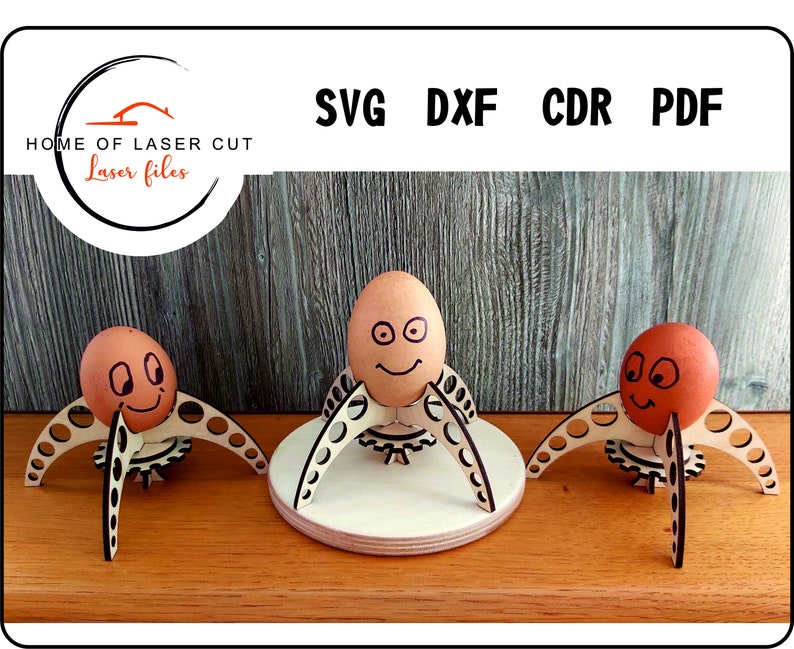 Puede incluir: Tres soportes para huevos de madera con un dise&ntilde;o de engranaje y un huevo marr&oacute;n con una cara dibujada en cada soporte. Los soportes est&aacute;n sobre una superficie de madera.