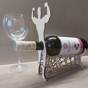 May include: Wooden wine bottle holder shaped like a person with arms raised in a muscle pose. The holder has a spiderweb design and is holding a bottle of Bollino Cherry wine.