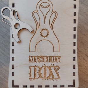 May include: A wooden box with a laser-cut design of an alien head and the words "Mystery Box".