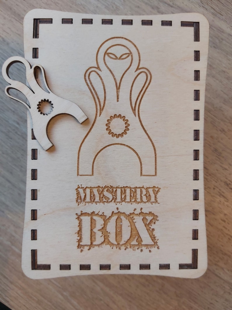 May include: A wooden box with a laser-cut design of an alien head and the words "Mystery Box".