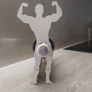 May include: Wooden wine bottle holder shaped like a person with arms raised in a strong pose. The bottle holder is made of light brown wood and is designed to hold a wine bottle.