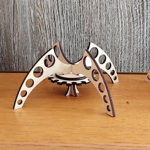 Puede incluir: Tres soportes geom&eacute;tricos de madera cortados con l&aacute;ser, con una base circular y tres patas curvas. Cada soporte tiene un patr&oacute;n circular de agujeros en las patas.