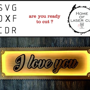 Puede incluir: Un letrero de madera con un borde iluminado, que presenta el texto "I love you" en una fuente decorativa. El letrero está hecho para corte por láser y está disponible en los formatos SVG, DXF y CDR.