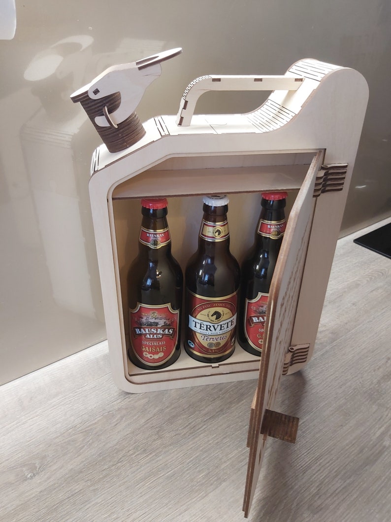 Puede incluir: Una caja de madera con forma de bid&oacute;n de gasolina con una puerta con bisagras. La caja est&aacute; llena de tres botellas de cerveza, dos etiquetadas como "Bauskas Alus" y una etiquetada como "Tervete Tervete".
