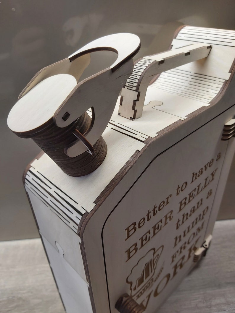 Puede incluir: Caja de madera con tapa con bisagras y asa. La caja tiene forma de bid&oacute;n de gasolina y tiene el texto "Mejor tener una BARRIGA DE CERVEZA que una joroba del TRABAJO" grabado en el lateral.