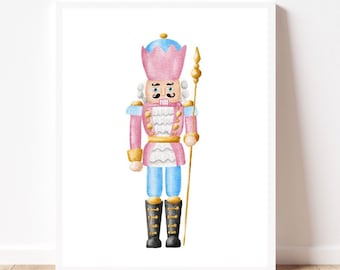 May include: A framed watercolour print of a toy nutcracker soldier. The nutcracker is in pink, blue, and gold, with black boots and a gold staff. The print is displayed on a white wall above a wooden floor.
