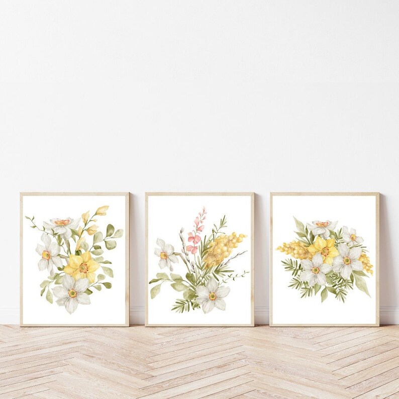 May include: Set of three watercolour prints featuring yellow and white floral bouquets with green leaves on a white background. The prints are framed in a light wood frame.