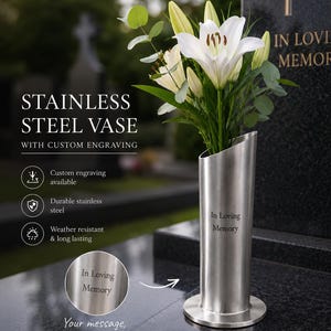 Könnte beinhalten: Eine zylindrische Vase aus Edelstahl mit schräger Öffnung und der Gravur In Loving Memory. Die Vase ist mit weißen Lilien und grünem Blattwerk bestückt und zeichnet sich durch ihr langlebiges und wetterbeständiges Design aus.