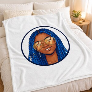 Könnte beinhalten: Weiße Fleecedecke mit einem kreisförmigen Motiv einer lächelnden Person mit blauen Zöpfen, goldfarbener Sonnenbrille und sternförmigem Haarschmuck. Das Motiv ist von einem dunkelblauen Kreis umrandet.