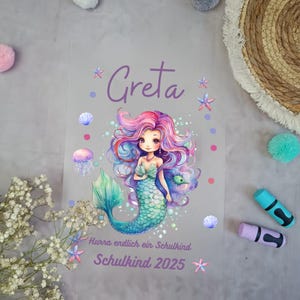 Könnte beinhalten: Eine lila und blaue Meerjungfrauen-Illustration mit dem Namen Greta und dem Text "Hurra endlich ein Schulkind Schulkind 2025".