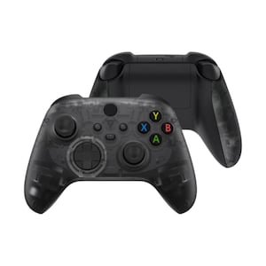 May include: Two black game controllers. One controller is transparent, revealing internal components. The other controller is solid black. The transparent controller has colored buttons: green, blue, yellow, and red. The controllers are for gaming.
