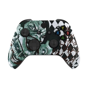 May include: A black and white Xbox controller with a unique design. The left side features a detailed green and white illustration of a monster, while the right side has a white and brown diamond pattern. The controller has black buttons and colored action buttons.