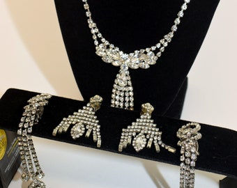 Op de afbeelding: Een vintage set met strass sieraden met een ketting, oorbellen en een armband. De set heeft een delicate ketting met een traanvormige hanger en hangende strass steentjes.