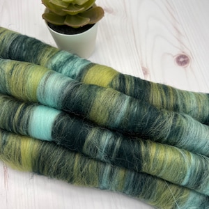 Può includere: Primo piano di un gomitolo di lana in tonalità di verde, blu e giallo. La lana è morbida e soffice, ed è perfetta per lavorare a maglia o all'uncinetto.