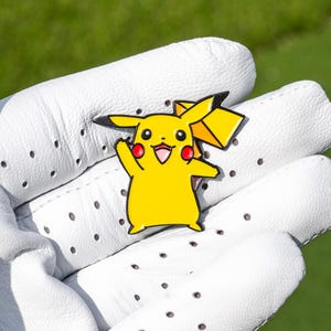 May include: A yellow enamel pin featuring the character Pikachu with black-tipped ears, red cheeks, and a lightning bolt-shaped tail. The character is depicted with a smiling expression, raised arm, and a bright yellow body, rendered in a flat, cartoon-style design with bold black outlines.