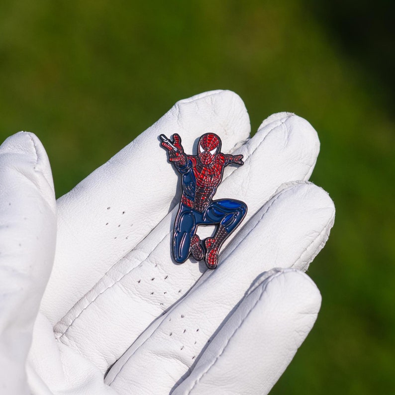 K&ouml;nnte beinhalten: Eine Emaille-Anstecknadel mit einem Cartoon-Bild von Spiderman in einer Sprungpose, mit roter und blauer Emaille.