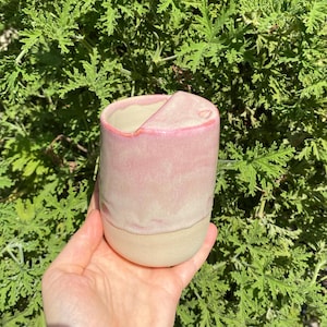Puede incluir: Una taza de cerámica rosa y blanca con un diseño único y asimétrico. La taza tiene un acabado liso y brillante y una forma ligeramente redondeada.