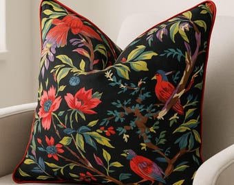 May include: Decorative throw pillow with a black background featuring a floral and bird design. The pillow has red trim and is filled with colorful flowers, leaves, and birds in shades of red, blue, yellow, and green.