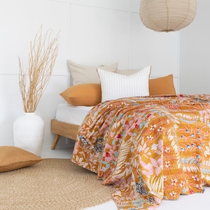 May include: A white bed with a floral patterned quilt and a tan rug. The bed has a white headboard and a tan lampshade hanging above it.