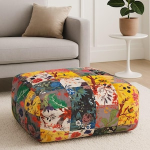 Könnte beinhalten: Ein quadratischer Hocker mit einem Patchwork-Design mit floralen und botanischen Mustern in verschiedenen Farben. Der Hocker steht auf einem weißen Teppich in der Nähe eines grauen Sofas und eines kleinen Beistelltisches mit einer Topfpflanze.