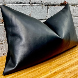 May include: A black leather cushion with a smooth, shiny finish. The cushion is rectangular and has a slight curve in the middle.