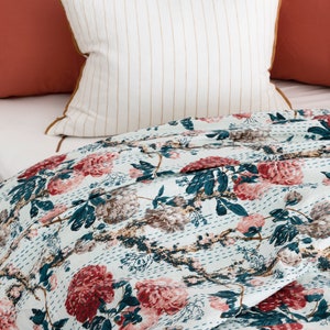 May include: A white and blue floral patterned quilt with a white pillow with brown stripes and a coral coloured pillow. The quilt is made of cotton and has a hand-stitched design.