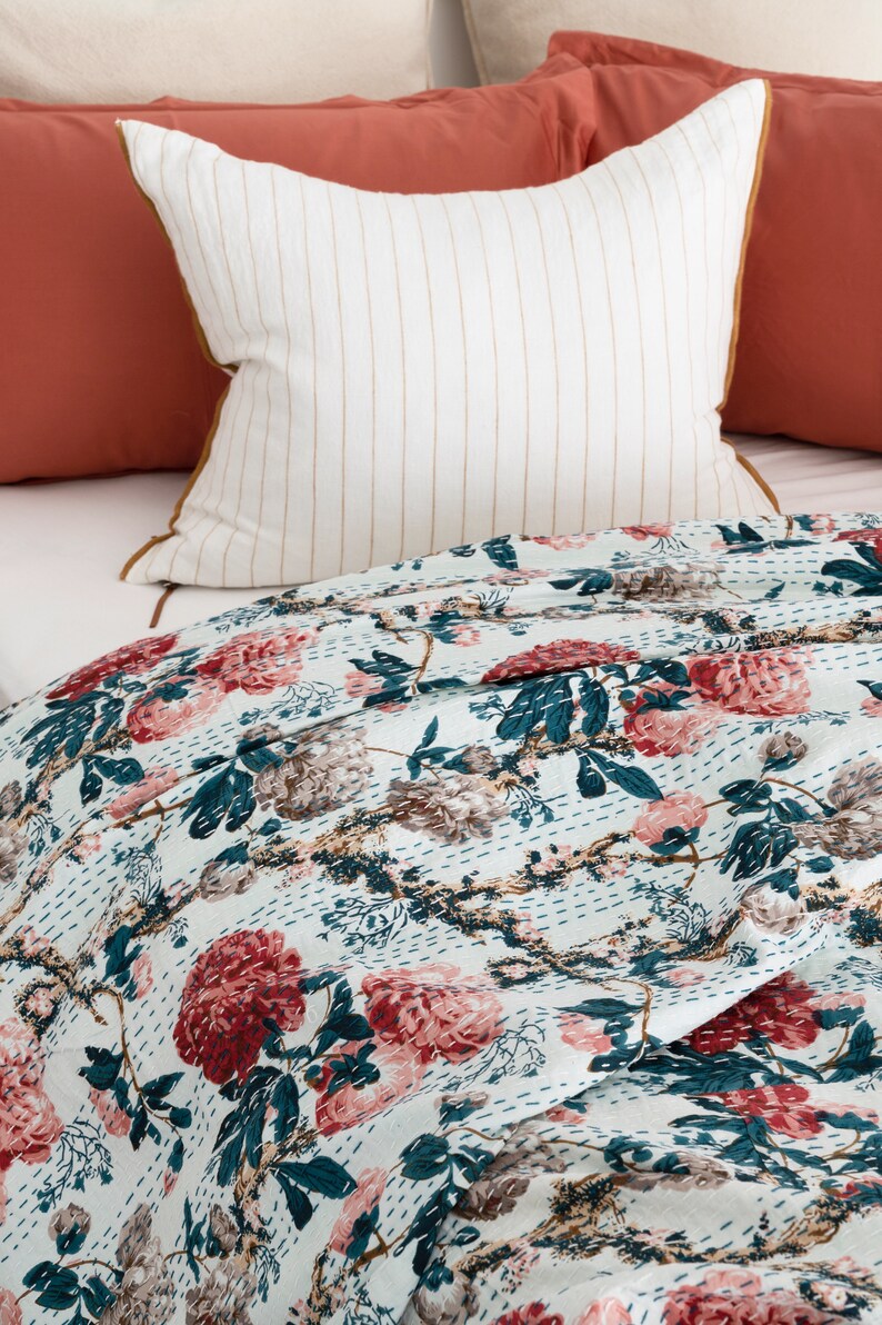 May include: A white and blue floral patterned quilt with a white pillow with brown stripes and a coral coloured pillow. The quilt is made of cotton and has a hand-stitched design.