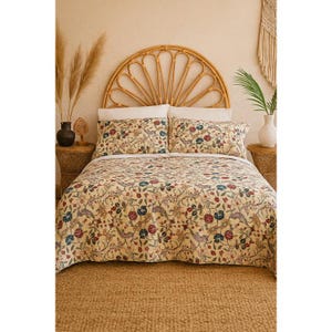 May include: A bed dressed with a cream-coloured duvet cover and pillowcases, adorned with a floral pattern in red, blue, and green. The room includes a woven headboard and a woven rug, creating a warm, inviting atmosphere.