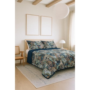 以下が含まれることがあります： ペイズリー柄のキルトと、お揃いの枕カバー2つが付いたベッド。キルトは、緑、オレンジ、青の色合いのカラフルなペイズリーのデザインが施された濃い青色の背景が特徴です。ベッドは濃い青色のシーツで構成されています。