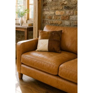 Peut inclure: Un canapé en cuir marron avec un coussin patchwork. Le coussin présente des carrés de marron et de crème. La pièce a un mur de briques et un cadre de fenêtre en bois.