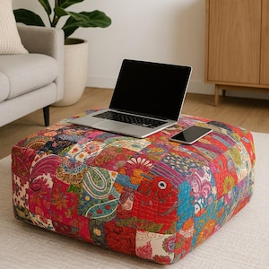 May include: A square, patchwork ottoman with a vibrant mix of floral and paisley patterns in red, blue, and yellow. A laptop and smartphone rest on top. The ottoman is a decorative furniture piece.
