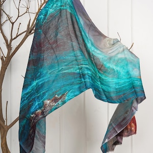 May include: A teal, blue, and gray patterned scarf with a wave design. The scarf is draped over a branch.