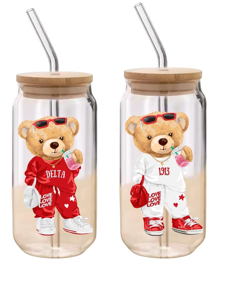 Puede incluir: Dos vasos de vidrio transparente con tapas de madera y pajitas de vidrio. Cada vaso presenta un oso de peluche de dibujos animados con gafas de sol y un ch&aacute;ndal. Un oso viste de rojo, el otro de blanco. El texto incluye "DELTA", "1913" y "LOVE LOVE LOVE".