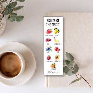 Puede incluir: Un marcapáginas blanco con ilustraciones de acuarela de frutas que representan cualidades espirituales. El texto "FRUITS OF THE SPIRIT" está en la parte superior, con la referencia bíblica Gal 5:22,23 en la parte inferior. Una taza de café y una planta están en el fondo.