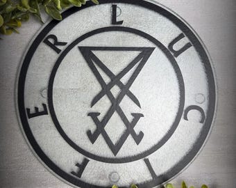 May include: A circular glass chopping board featuring a black Sigil of Lucifer centred within a black circular border. The letters L, U, C, I, F, E, R are printed in black around the perimeter of the circle. The glass has a textured, frosted finish.