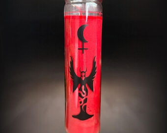 May include: A tall, cylindrical glass candle filled with bright red wax. The front of the glass features a black graphic print consisting of a crescent moon positioned above a cross symbol, with a winged figure standing above a coiled snake.
