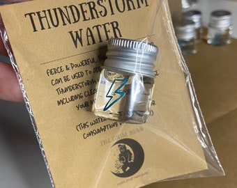 May include: A small glass bottle with a silver lid containing clear liquid. The bottle has a lightning bolt sticker on it. The bottle is labeled "Thunderstorm Water" and "Fierce & Powerful This Can Be Used To Add Thunderstorm Including Clean Your Im (This Water Consumption! The Crim Bear Make Your Own Path"