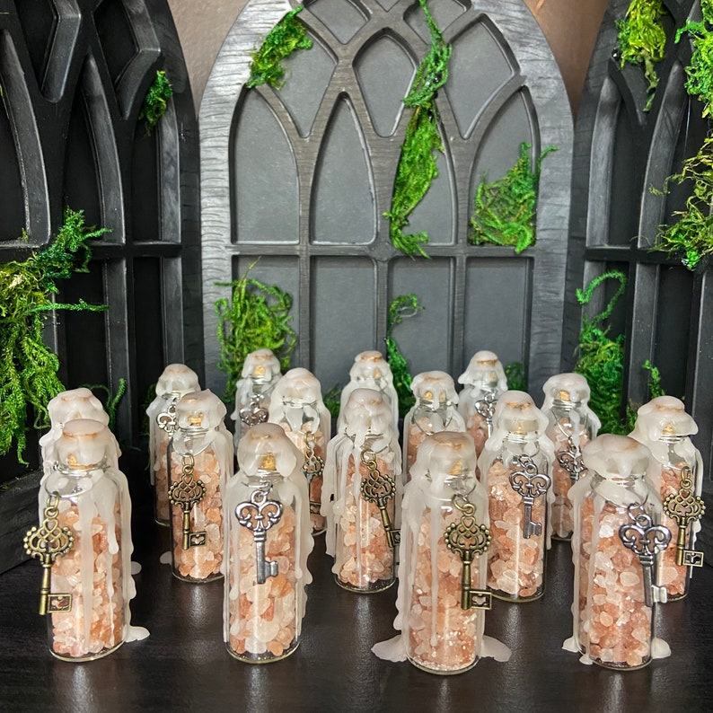 May include: A collection of small glass bottles filled with pink Himalayan salt and topped with a wax seal. Each bottle features a small silver key charm hanging from the wax seal.