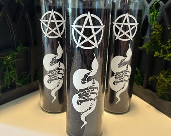 May include: Three black glass candle jars with white pentagram and snake designs. The candles are filled with black wax.