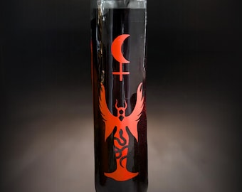 May include: A tall, cylindrical glass candle container filled with dark wax. The front features a bright orange graphic print consisting of a crescent moon positioned above a cross symbol, followed by a winged figure with a serpent-like body design.