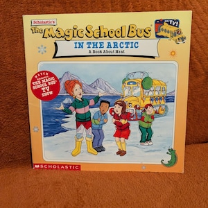Op de afbeelding: Een Scholastic-boek The Magic School Bus In The Arctic over warmte. De kaft bevat een illustratie van een leraar en drie leerlingen in een besneeuwd landschap bij een gele bus met rupsbanden, met een rode cirkelvormige badge met de tekst Watch The Magic School Bus TV Show.