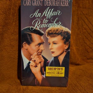 May include: A VHS tape of the film "An Affair to Remember" starring Cary Grant and Deborah Kerr. The cover art depicts the actors in a romantic pose. The tape is in a plastic case with a promotional sticker.
