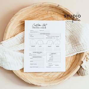 May include: A white "Custom Hat Order Form" on a wooden tray. The form includes sections for customer details, sizing, design details, and order information. The Studio Flutter logo is in the upper right corner. A white cloth is draped around the form.
