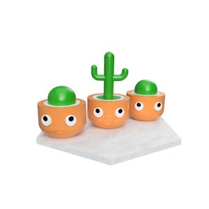 Peut inclure: Trois pots de fleurs orange avec des accents verts et des visages expressifs. L'un contient un cactus vert, les autres des dômes verts. Les pots sont sur une surface blanche.