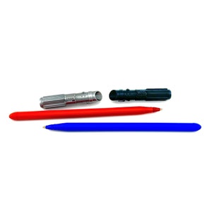 Puede incluir: Tres bol&iacute;grafos, dos rojos y uno azul, est&aacute;n dispuestos en fila. Los bol&iacute;grafos rojos tienen forma de sable l&aacute;ser y tienen tapas plateadas. El bol&iacute;grafo azul es un bol&iacute;grafo de tinta de bola est&aacute;ndar.