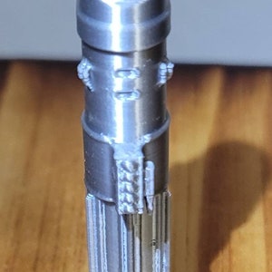 May include: A silver-colored lightsaber prop with a detailed handle and a rounded tip.