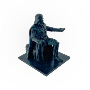 May include: A black 3D printed figurine of Darth Vader kneeling on a black base. The figurine is detailed and realistic, with a cape and a lightsaber.