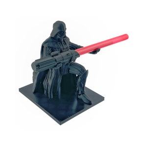 May include: A black 3D printed figurine of Darth Vader kneeling and holding a red lightsaber. The figurine is on a black base.